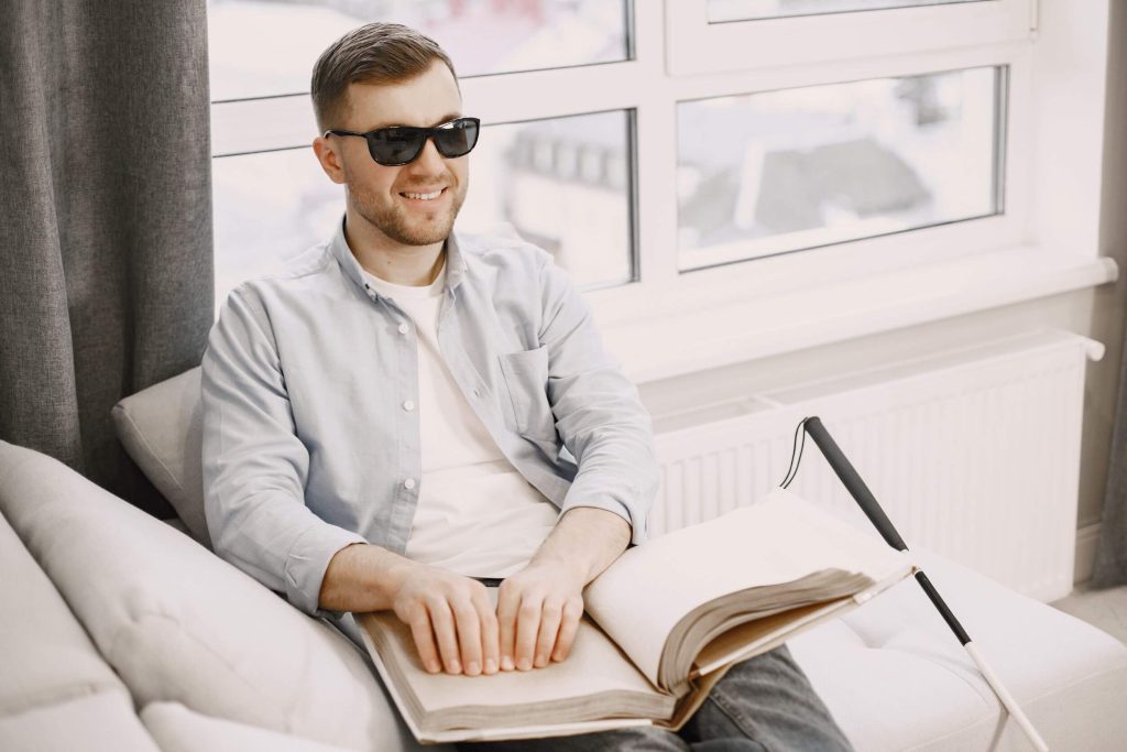 blind young man reading braille book on couch