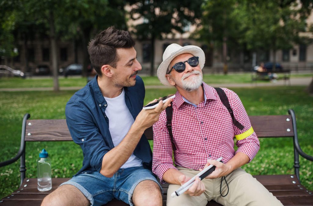 young man and blind senior sitting on bench in park
